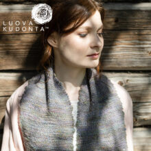 malli seisoo ruskean hirsiseinän edessä, kaulassa Kanervikko-huivi