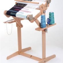 Rigid-heddle-loom-jalustan-hyllyt-luova-kudonta Pirtakangaspuut jalustaan kiinnitettynä, hyllyillä sukkula, sakset ja kaksi lankakartiota.